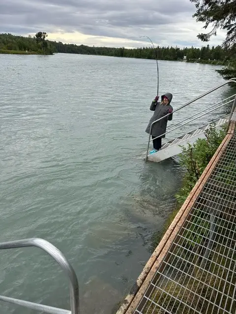 An angler on a river platform with the Kenai behind