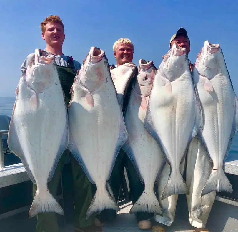 Four guests on the deck of a Cook Inlet charter holding up their halibut